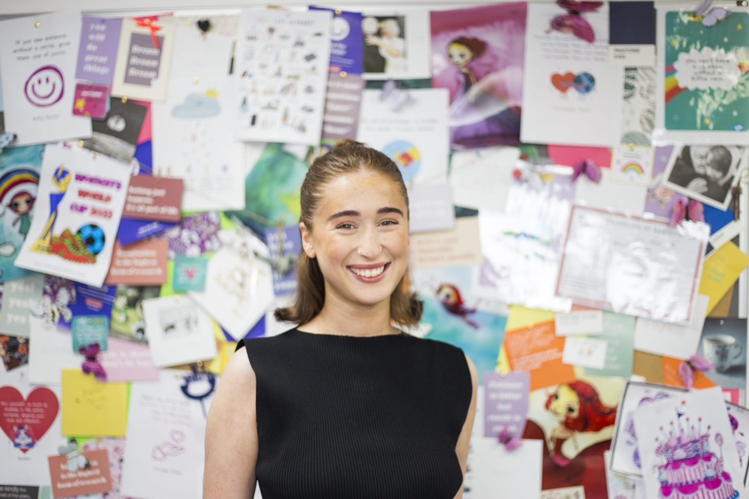Jess, a PA at Face For Business, smiling in front of a noticeboard